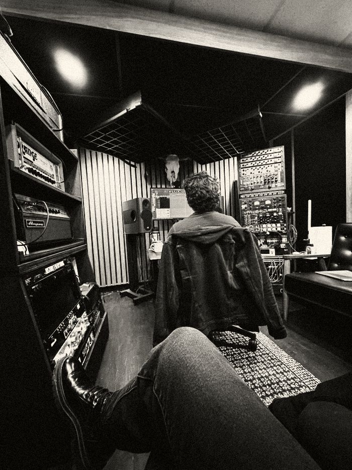 Black-and-white photo from the Rat Park sessions at Riff Audio: boots up in the foreground, the engineer at the mixing desk facing the monitors, amps and racks of outboard gear on either side.